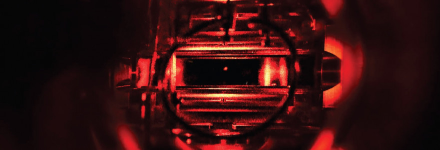 Zdjęcie wnętrza układu doświadczalnego w wysokiej próżni. Jasny punkt w centrum to chmura ultrazimnych atomów otoczona elektrodami, które trzymają jon. Fot.: Uniwersytet we Fryburgu.